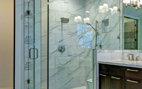 Modern bathroom with glass shower, marble walls, and dark wood vanity with a marble countertop.